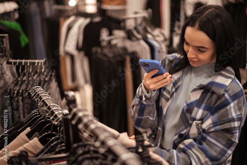 Beautiful brunette girl scanning barcode with her smartphone in clothes store