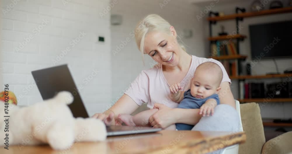 Cheerful mother holding her baby son and working on the laptop Cheerful mother holding her baby son and working on the laptop