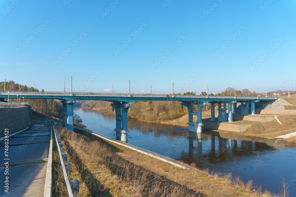 Fototapeta premium A new modern automobile bridge over the river on the background of the blue sky. A sturdy reinforced concrete bridge, thick concrete arches and metal floors.