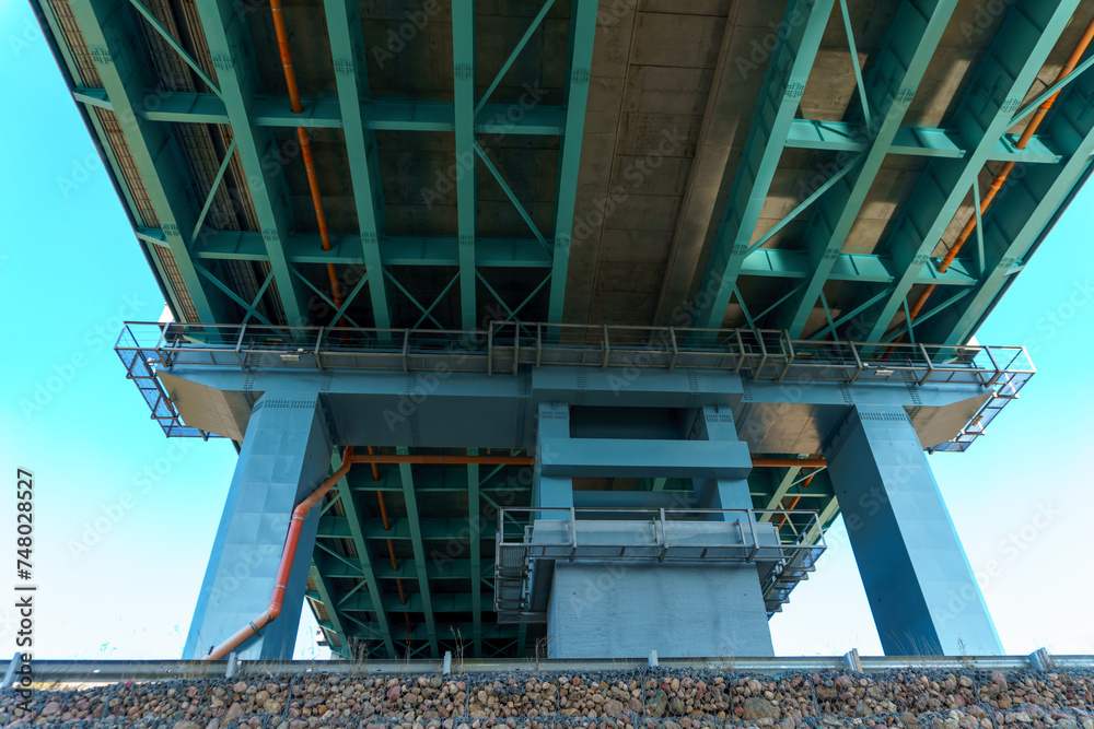 Parts of a modern metal bridge in close-up against a blue sky background. Metal structures connected by large bolts and nuts to a reinforced concrete base. Railway or automobile bridge.