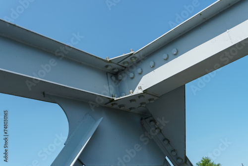 Parts of a modern metal bridge in close-up against a blue sky background. Metal structures connected by large bolts and nuts to a reinforced concrete base. Railway or automobile bridge.