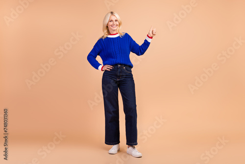 Full body photo of pretty cheerful person arm finger demonstrate thumb up empty space ad isolated on beige color background