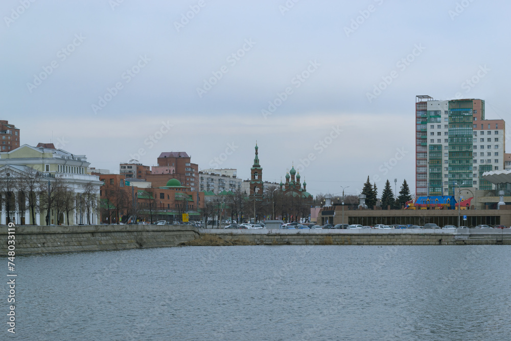 A city landscape with a river and various buildings on a cloudy day