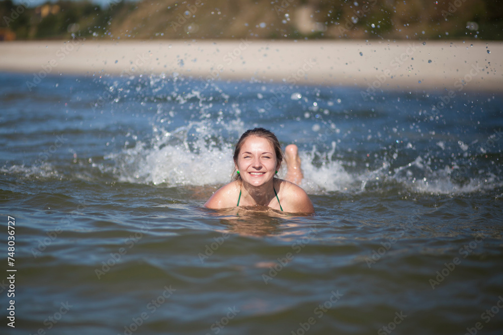 A woman splashes in the water, splashes flying in all directions. The woman smiles broadly and screams from the cold water