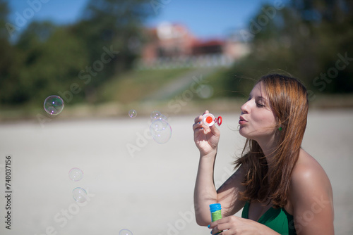 A woman in a green bikini swimsuit launches soap bubbles on the beach