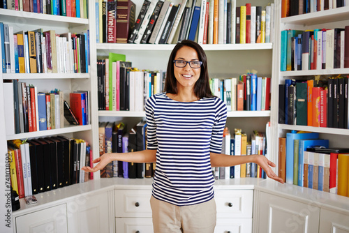 Woman, portrait and confidence by bookshelf in home with books for reading, learning or knowledge in living room. Person, face and happy by library in house with magazine, journal or study collection