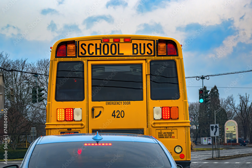 You never really realize just how tall a school bus is until you see it in comparison to a compact car. Yellow School Bus at Intersection waiting to turn Left.