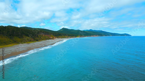 Top view of coastline of coast with mountains on horizon. Clip. Island with green forest and mountains on ocean coast. Paradise place to relax in wild on coast of island with mountains