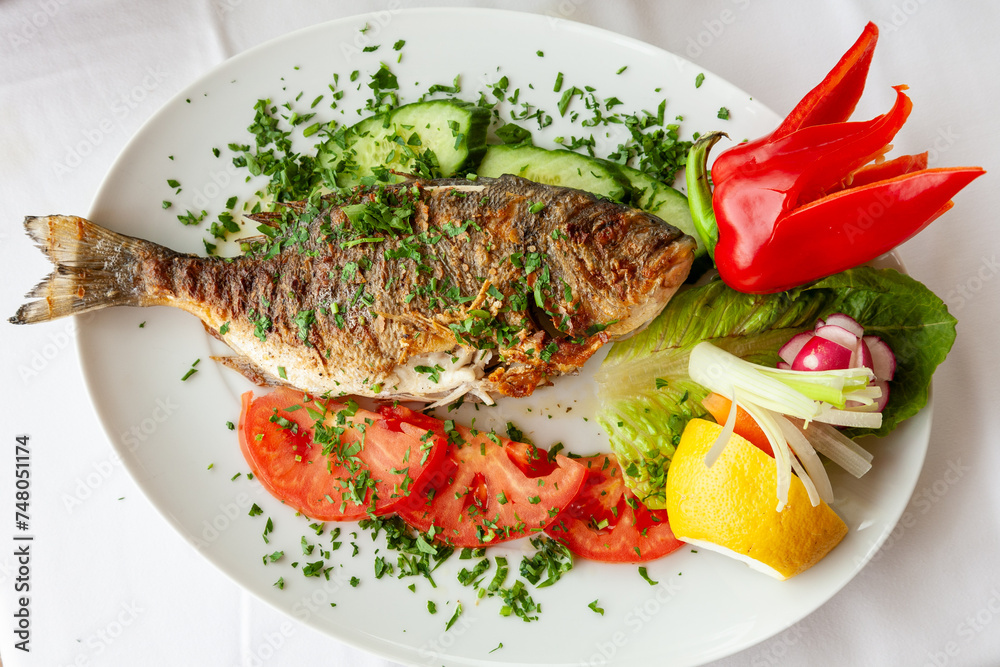 Grilled dorado fish served on a white plate with vegetables and lemon. Grilled dorado fish served on a white plate with vegetables and lemon.