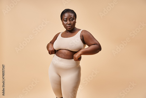 plus size woman in underwear posing on beige backdrop, body positive and female empowerment