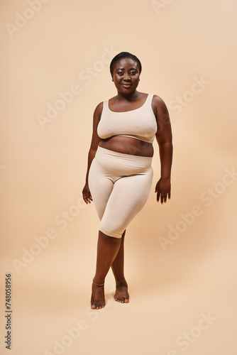 plus size african american model in beige attire posing against a matching backdrop, body positive