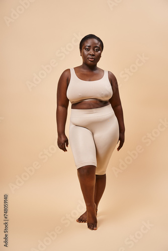 Graceful plus size african american model in beige attire posing against a matching backdrop