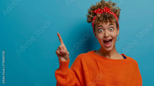An excited woman with curly hair and a red headband points upwards, her eyes wide and mouth open in a moment of joyful realization against a teal background.