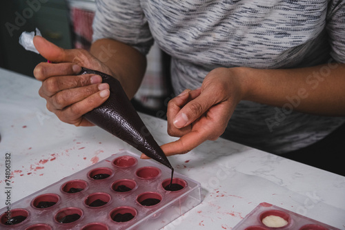 A chef or chocolatier prepares sweet chocolates at home. Close-up of the chocolatier's hands pouring chocolate into the molds. The chef's pastry bag pours hot melted chocolate into a plastic mold.