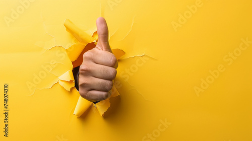 A hand is breaking through a yellow paper background giving a thumbs-up gesture, symbolizing approval or a positive response.