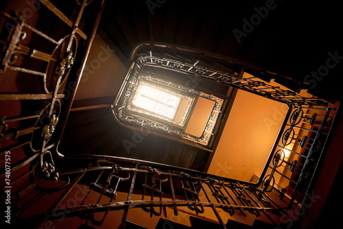 Looking up at the spiral staircase in old house. Dark staircase filled with warm interior light. 