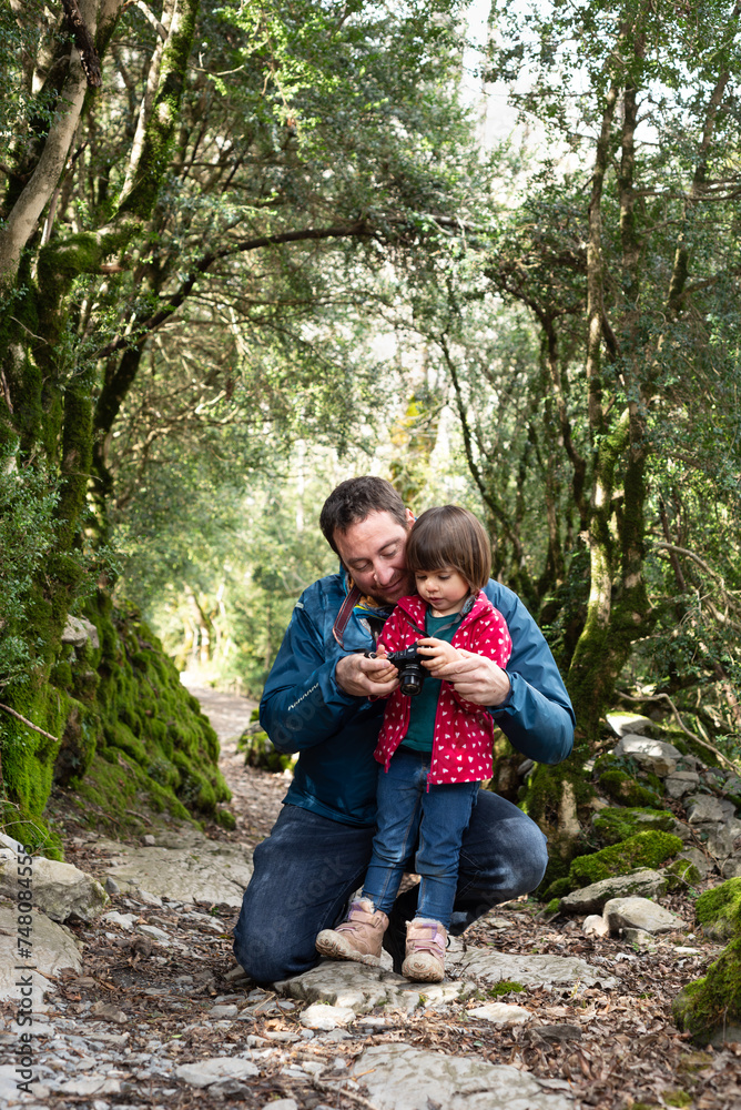 Father teaching photography to his little daughter during a hiking day in a pyrenean forest. Father teaching photography to his little daughter during a hiking day in a pyrenean forest.