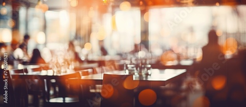 A blurred image of a restaurant interior, showcasing tables and chairs set up in the space. The background features a bokeh effect, adding a soft focus to the scene.