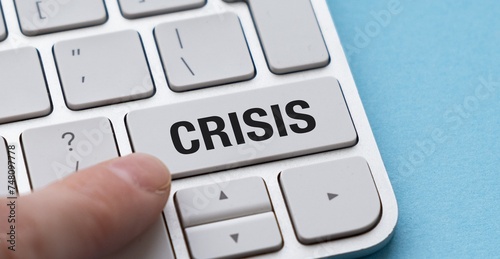 Finger pressing a white keyboard with the word crisis in red letters.