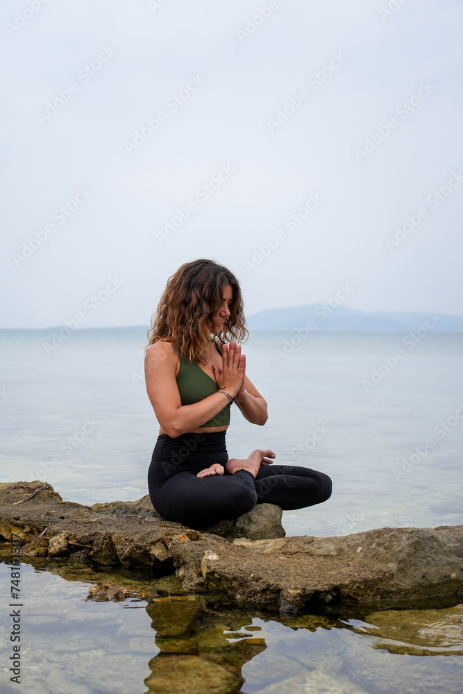 Woman practicing yoga by the sea on the rocks