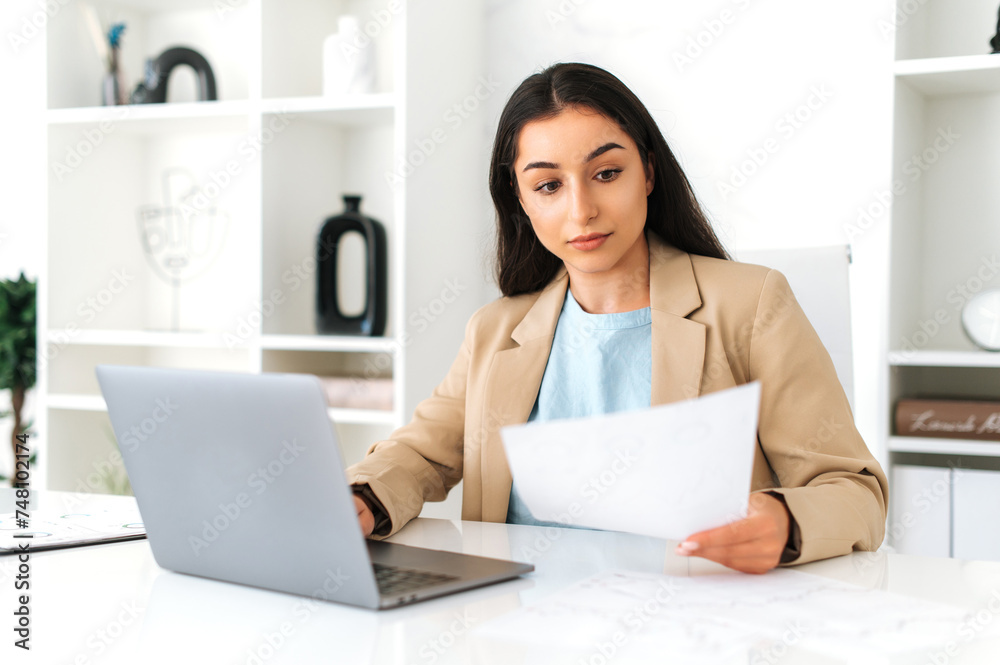 Work with documents. Focused serious indian or arabian business woman, financial manager, sit at workplace in the office with laptop, concentrated studying documents, create business plan and strategy Work with documents. Focused serious indian or arabian business woman, financial manager, sit at workplace in the office with laptop, concentrated studying documents, create business plan and strategy