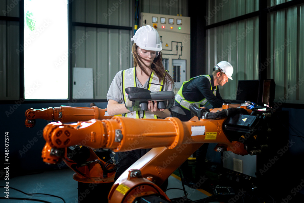 Fototapeta premium Factory engineers inspecting on machine with smart tablet. Worker works at heavy machine robot arm. The welding machine with a remote system in an industrial factory. Artificial intelligence concept.
