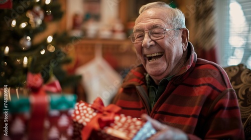 Elderly man laughs heartily as he opens a Christmas present surrounded by family