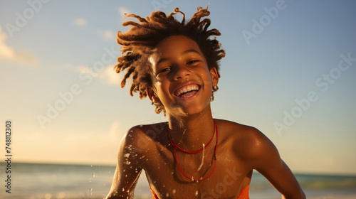 a young african american teenage happily enjoying himself on a sunny beach during a warm day. © OHMAl2T