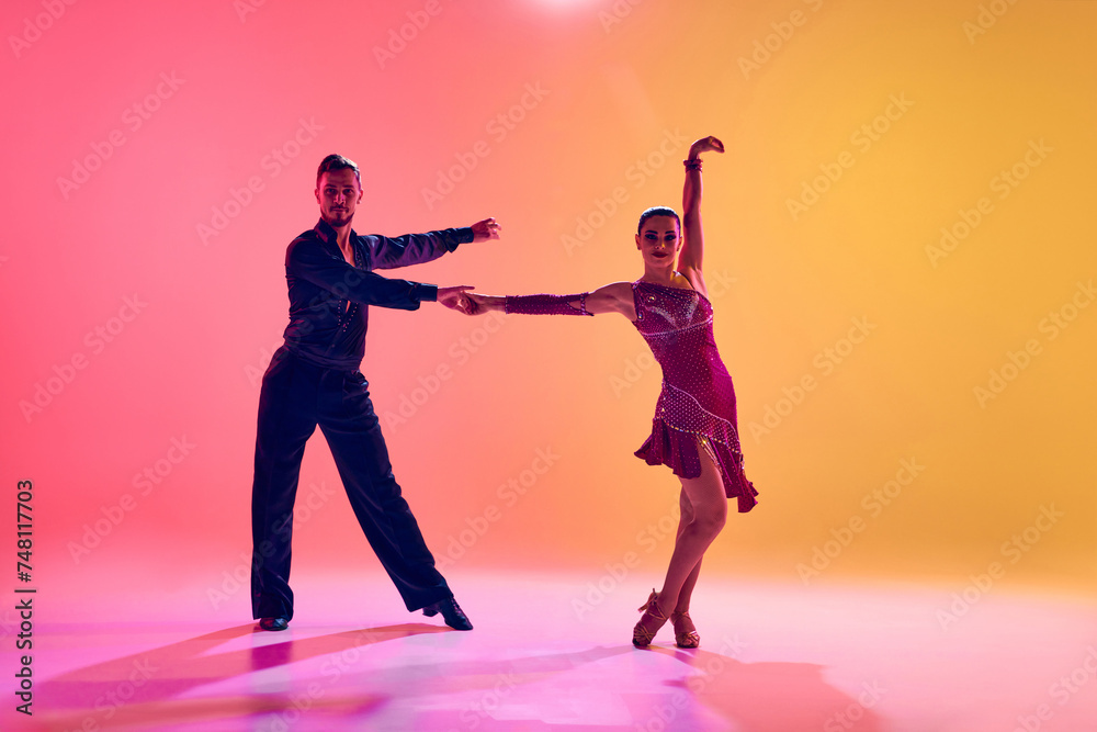 Male and female dancers performing a Latin dance in stylish clothes against gradient pink yellow background in neon light. Concept of dance class, hobby, art, dance school, talent Male and female dancers performing a Latin dance in stylish clothes against gradient pink yellow background in neon light. Concept of dance class, hobby, art, dance school, talent