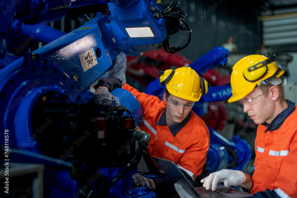 Factory engineers inspecting on machine with smart tablet. Worker works at heavy machine robot arm. The welding machine with a remote system in an industrial factory. Artificial intelligence concept. Factory engineers inspecting on machine with smart tablet. Worker works at heavy machine robot arm. The welding machine with a remote system in an industrial factory. Artificial intelligence concept.