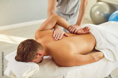 Male masseur or doctor physiotherapist making back massage for male young patient lying on the couch in modern rehabilitation clinic. Osteopathic medicine and physical rehab concept.