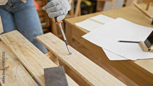 Caucasian woman in casual attire performing carpentry work with chisel and wood in a well-lit workshop. photo