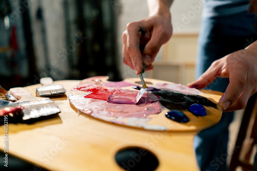 close up in an art studio an artist mixes paint on a palette with a palette knife