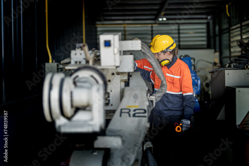 Engineer man checking the status of machine and used wrench to screw some part of equipment at CNC factory. Worker wearing safety glasses and helmet. Maintenance and repairing concept. © ultramansk
