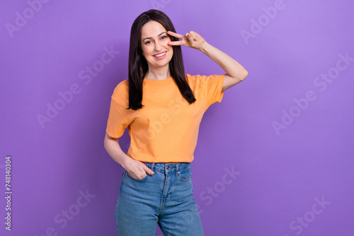 Portrait of good mood pleasant girl wear oversize t-shirt showing v-sign on eye holding palm in pocket isolated on violet color background