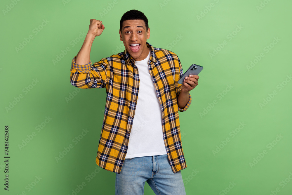 Photo of young guy winning a bet using smartphone online casino poker stars company raised fist up isolated on green color background Photo of young guy winning a bet using smartphone online casino poker stars company raised fist up isolated on green color background