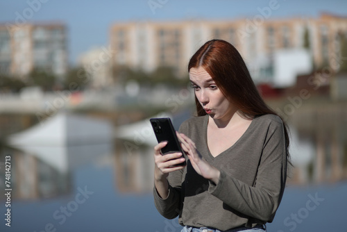 Young woman looks surprised at her phone in a park on a sunny day