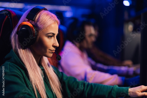 Female gamer with pink hair playing multiplayer video game with diverse friends
