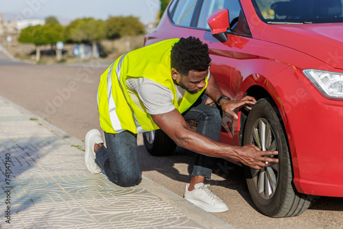 African-American man checks the tire of a red car with a yellow vest