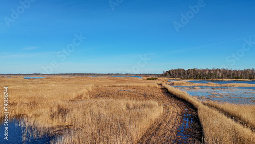 Wooden Bords Trail Through the Kaniera Lake Reeds Aerial Spring Shot Lapmezciems, Latvia. Frozen Lake and Baltic Sea in the Background. Early Spring in Latvia, Kemeri National Park. Slow Motion Shot