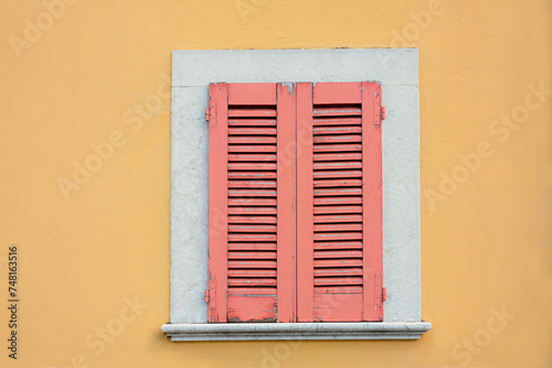 yellow house facade and window with closed red shutters, exfoliated paint © SusaZoom
