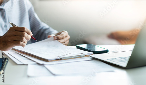 Asian businessman reviewing document reports at office workplace with computer laptop. legal expert, professional lawyer reading and checking financial documents or insurance contract before sign