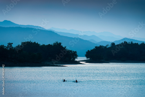 Blue scene of the Kaeng Krachan reservoir with fishing boat and tourist rowing canoe photo