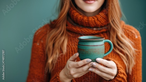 a close up of a person holding a cup in front of a teal green background with a scarf around her neck. photo