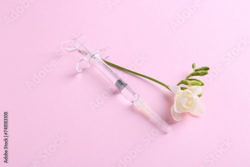 Cosmetology. Medical syringe and freesia flower on pink background