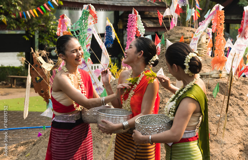 Pretty cheerful Thai women in traditionally Thai dresses holding silverware bowl splashing water to each other in Song kran festival in Chiangmai, Thailand