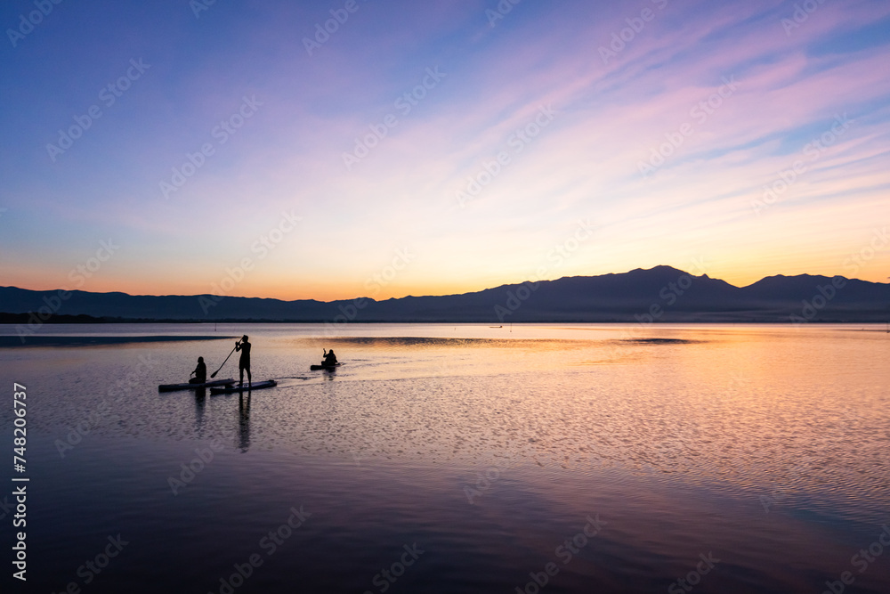 Silhouette of 3 people enjoy punting in  the lake at sun set