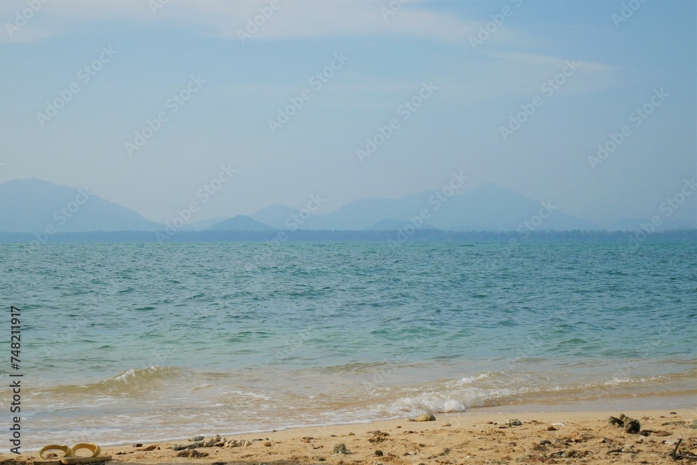 Sea, beautiful sandy beach slight wave Contrast the horizon line with mountains and sky.