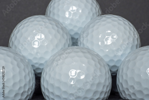 Close-up image of some plain white golf unbranded golf balls stacked up upon each other in front of a black background.