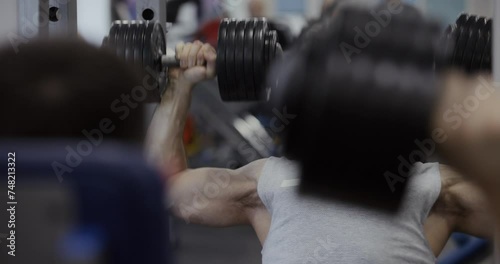 A man training deltoid muscles with dumbbells near mirror at the gym photo